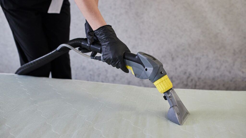 Cleaning service company employee removing dirt from furniture in flat with professional equipment. Female housekeeper arm cleaning the mattress on the bed with washing vacuum cleaner close up