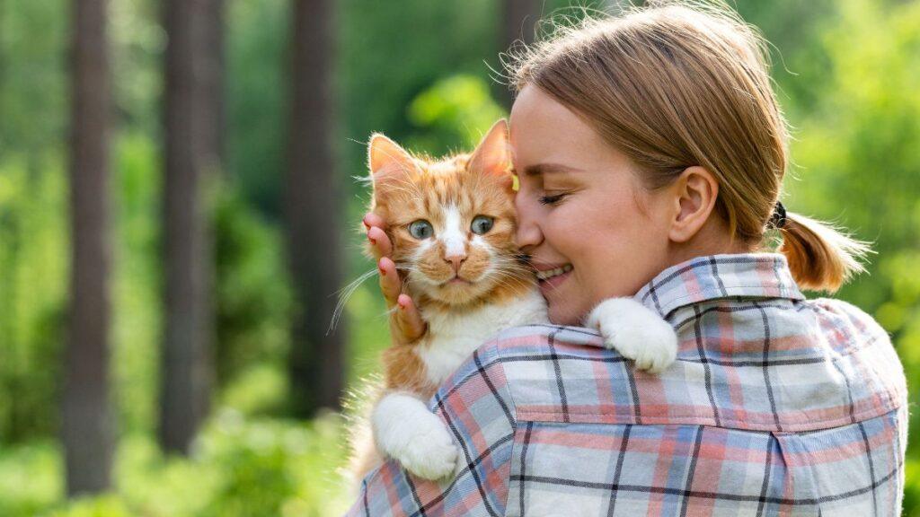 Woman holding a scared looking orange cat in the woods